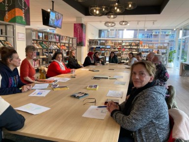 Foto met deelnemers van vertelvoorstelling aan de grote tafel in de bibliotheekvestiging Beverwijk