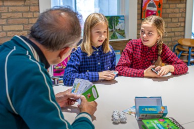 Afbeelding met grootvader en kleinkinderen samen spelletje spelen in de Bibliotheek